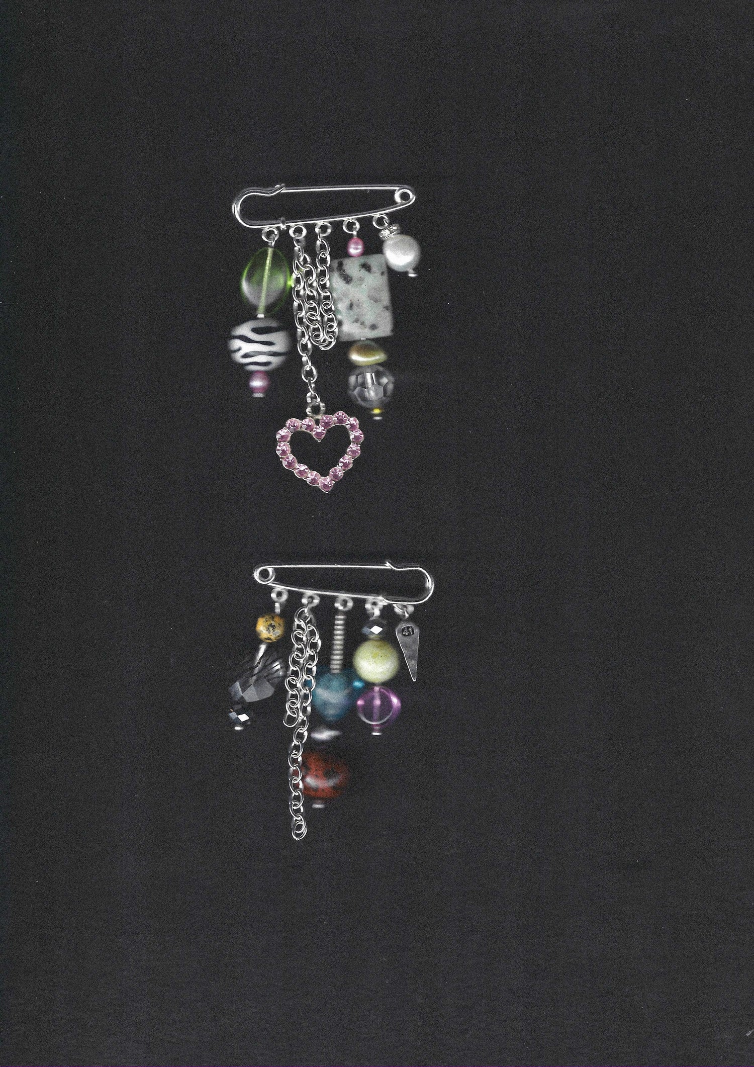 One-of-a-kind silver pin brooches with charms, beads, and chains on a black background.