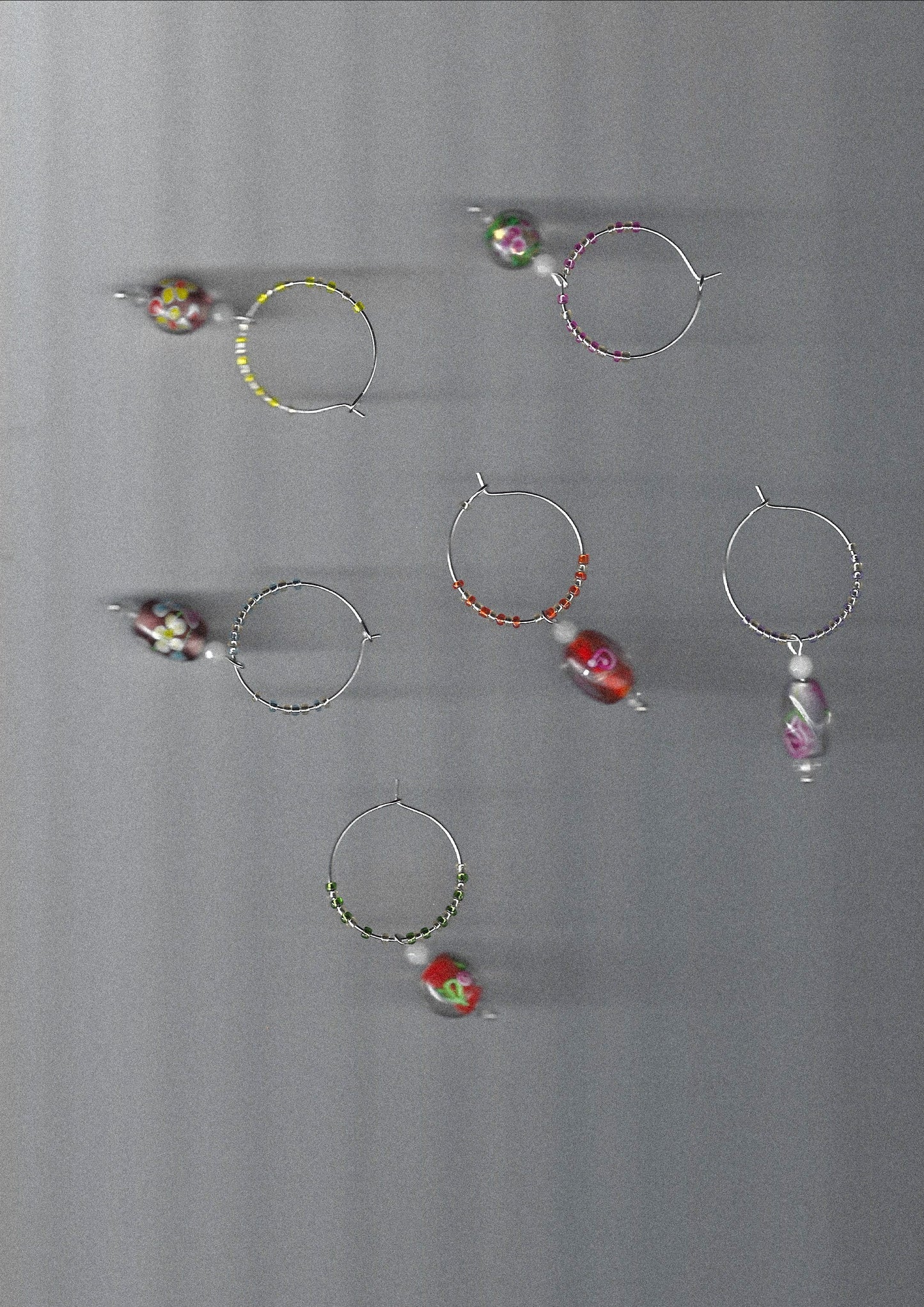 Set of wine glass charms with colorful floral beads on a gray background