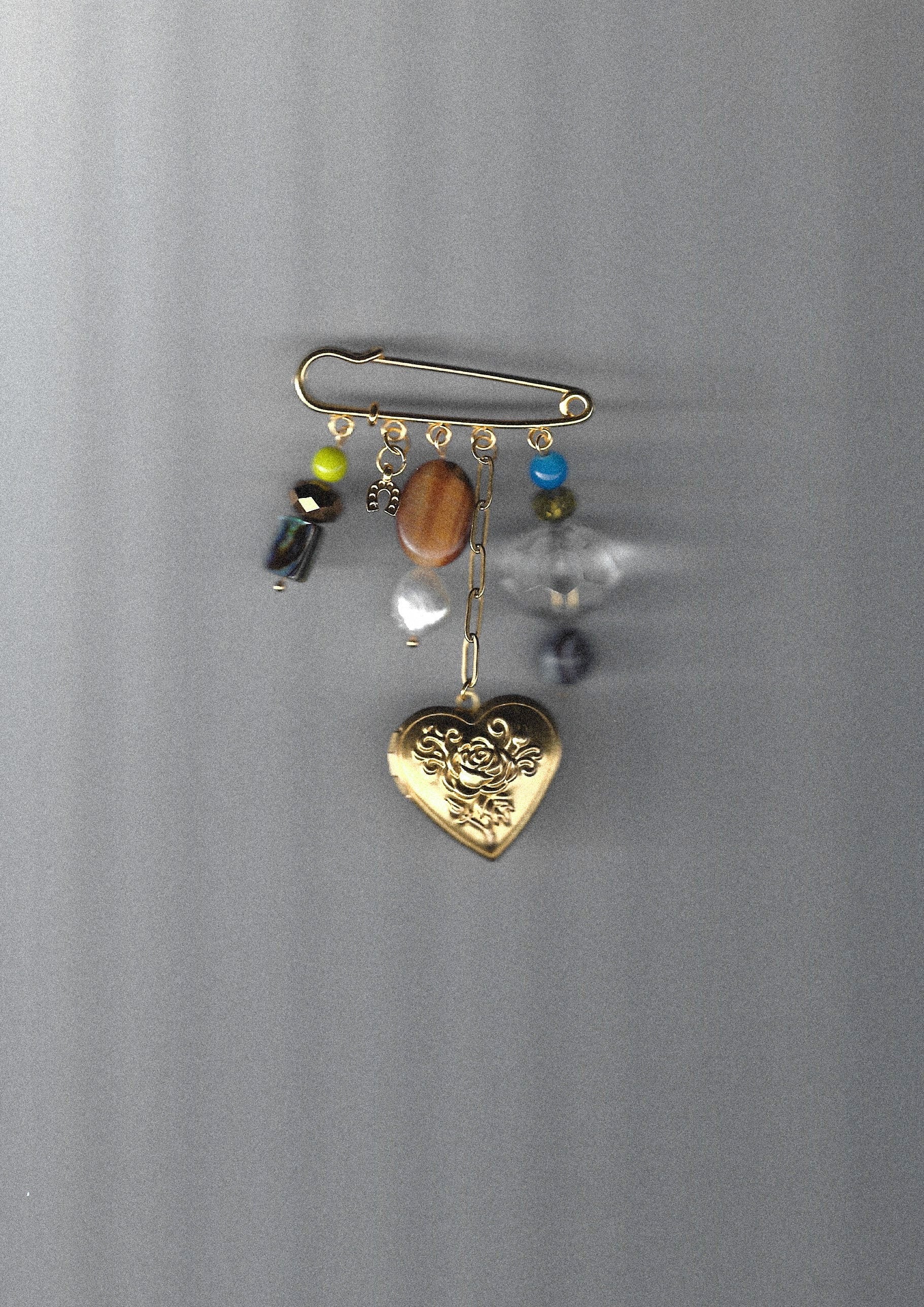 Gold heart-shaped pendant pin brooch with colorful beads on a plain background